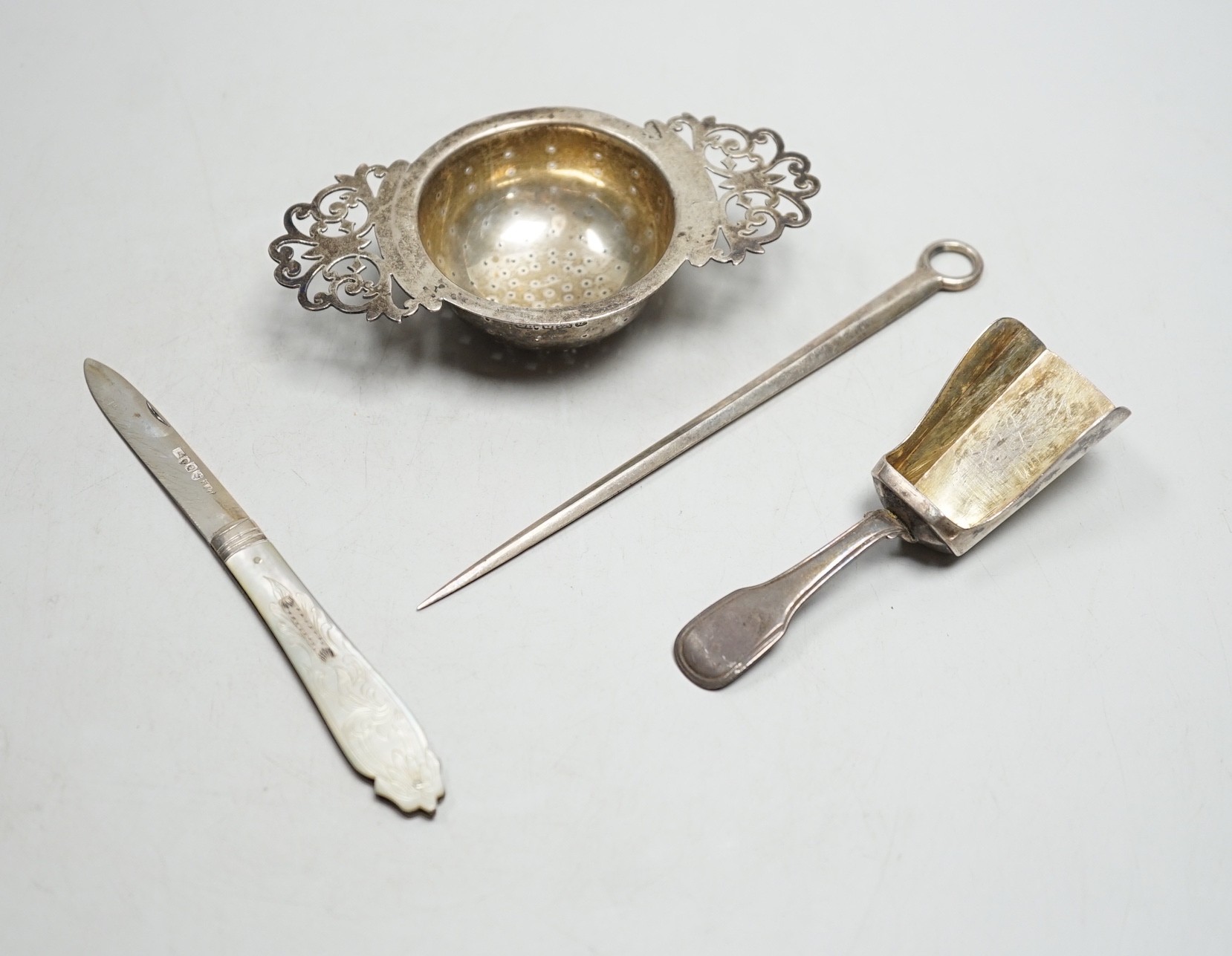 A silver tea strainer, a George III silver 'shovel' caddy spoon, London, 1811, a mother of pearl handled silver fruit knife and George IV silver game skewer, London, 1825, 14.7cm.